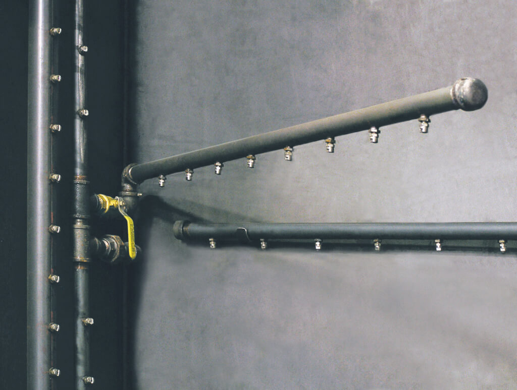 Closeup of a steel spray bar inside an aqueous parts washer.