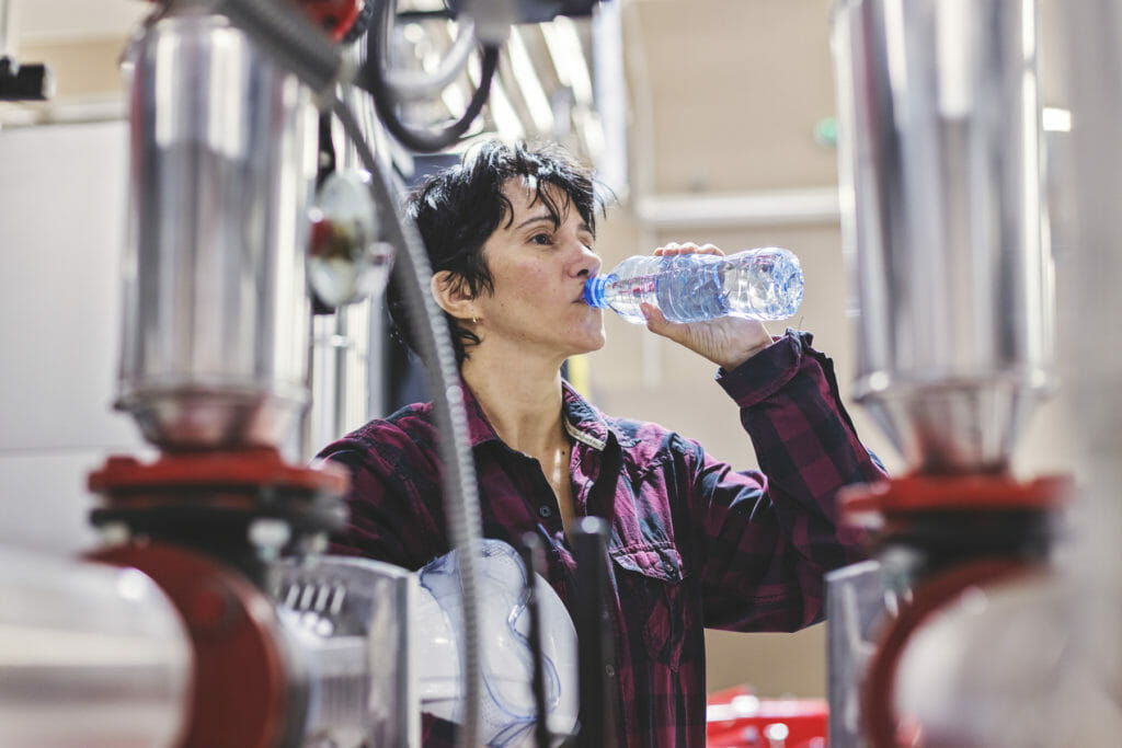 Female engineer at a fabrication shop drinks out of a water bottle to stay hydrated on hot days.